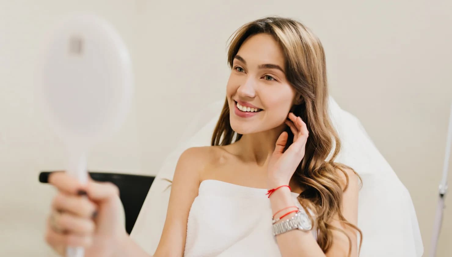 Smiling client looking at her reflection in a hand mirror in a treatment chair