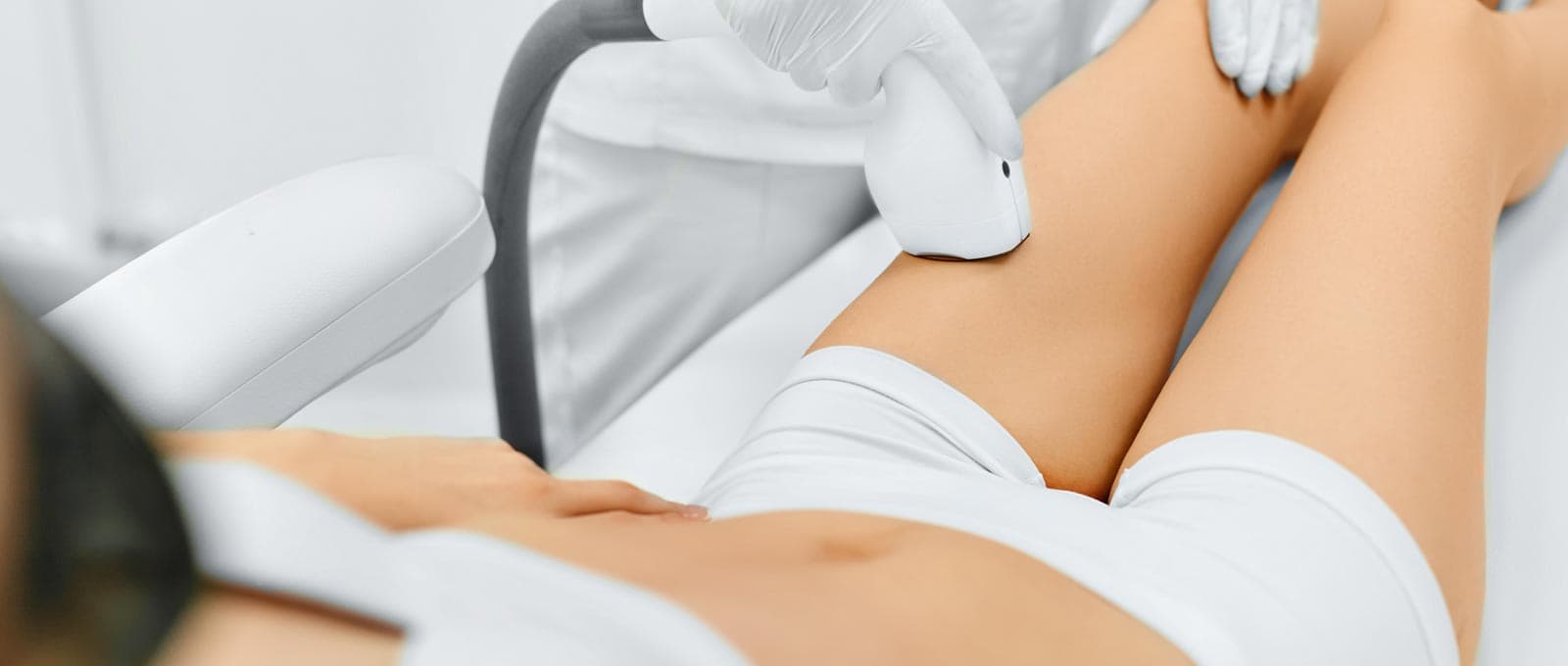 Practitioner in white gloves moving a laser handpiece along a client’s thigh during laser hair removal